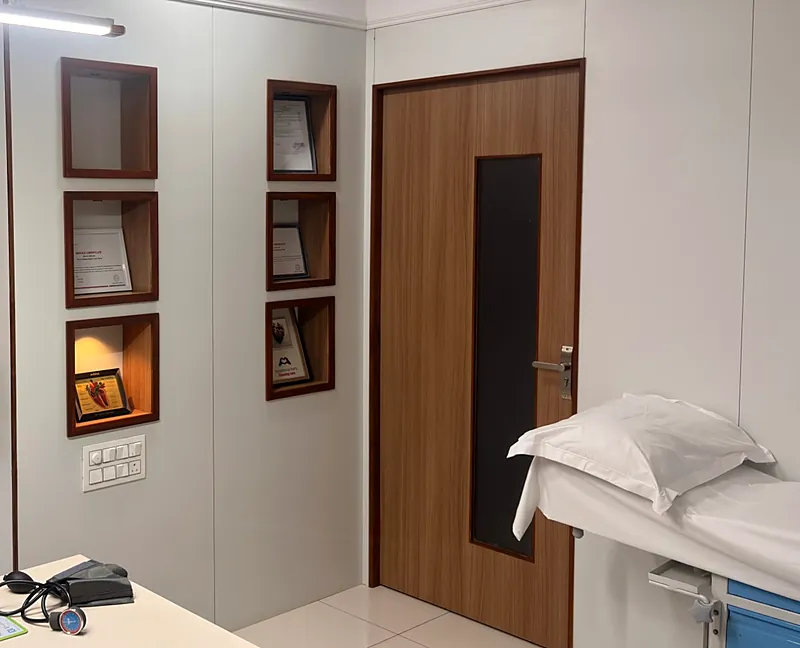 The consultation room: the doctor's desk, wall niches with framed certificates, and an examination bed beside the door